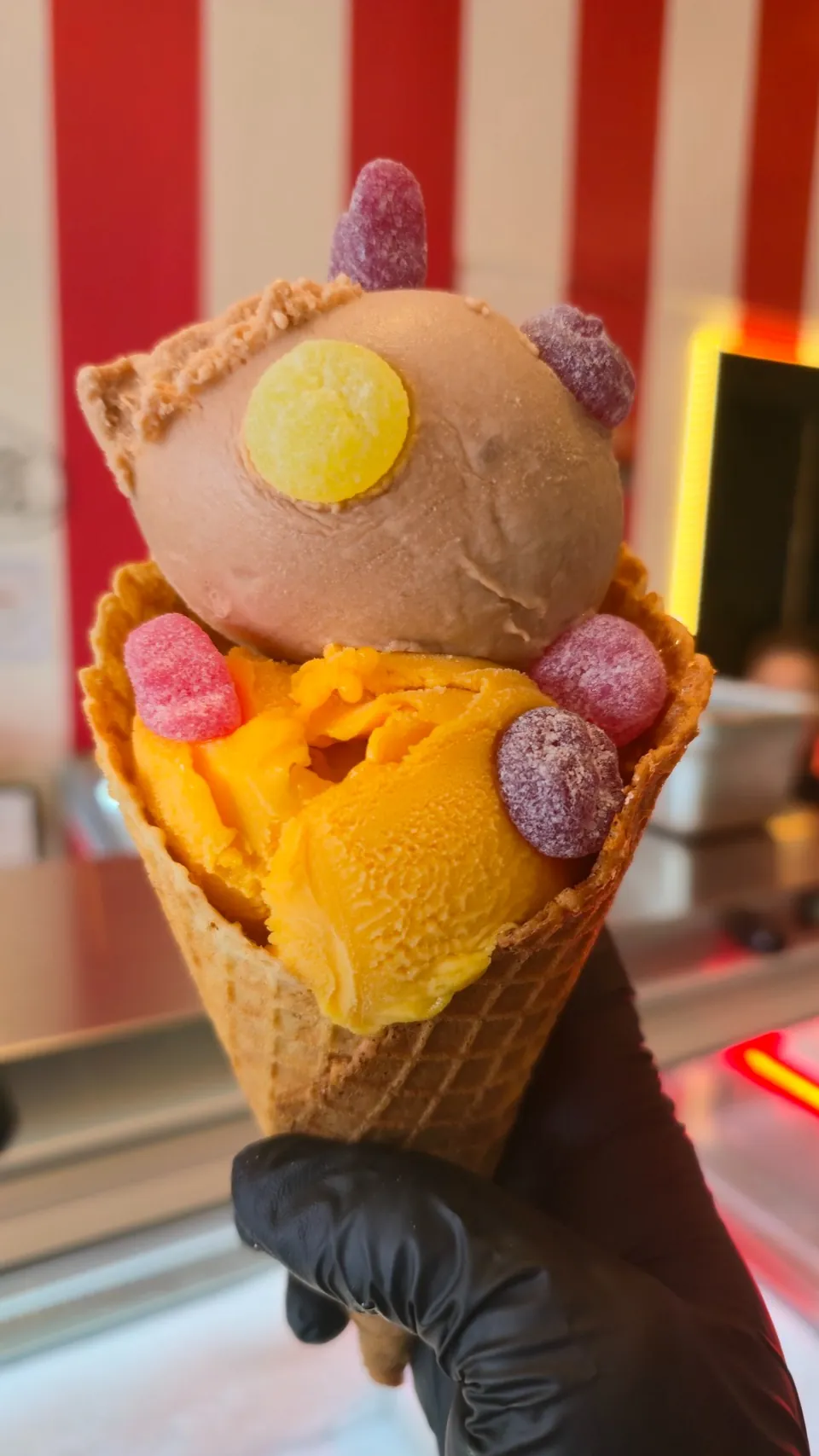 Double scoop waffle cone decorated with colorful candy against the parlor's red-stripe wall