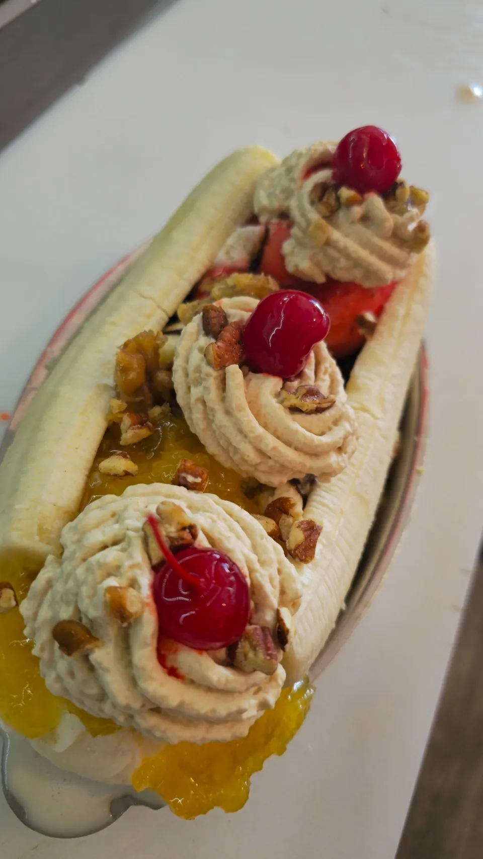 Overhead view of a banana split with three whipped cream scoops and maraschino cherries