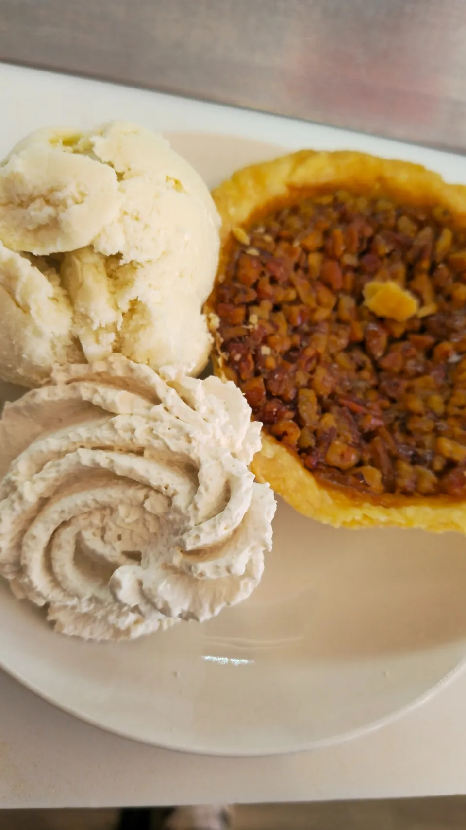 Homemade pecan pie slice served alongside vanilla ice cream scoops and cinnamon whipped cream