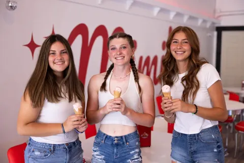 Three guests smiling with ice cream cones inside Mimi's Sweet Treats parlor