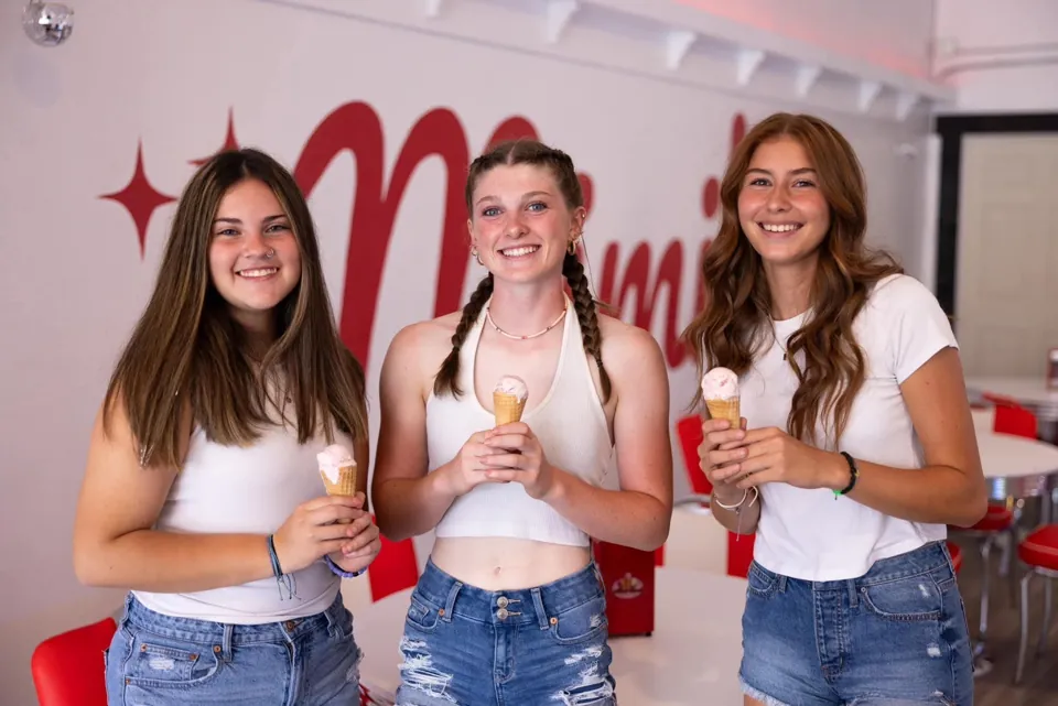 Three guests smiling with ice cream cones inside Mimi's Sweet Treats parlor
