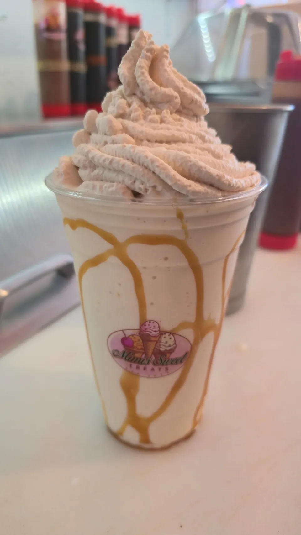 Caramel milkshake with swirled whipped cream in a branded Mimi's Sweet Treats cup