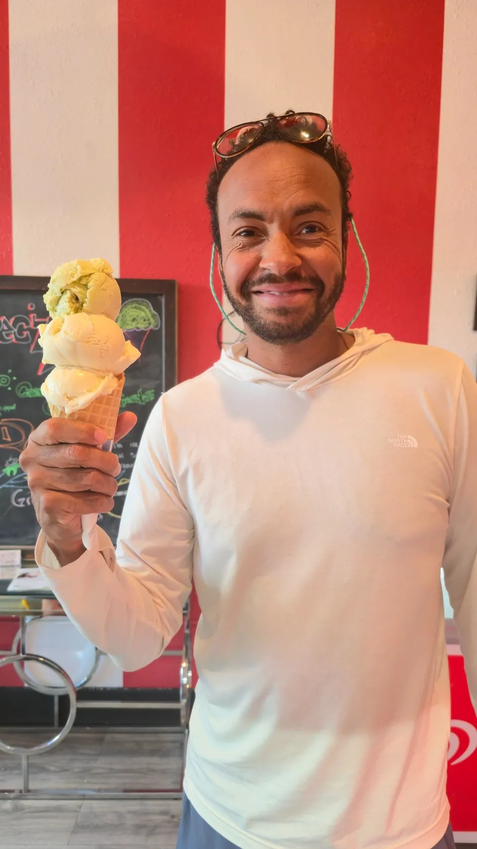 A smiling customer holding a double scoop waffle cone in front of Mimi's retro red-and-white striped wall