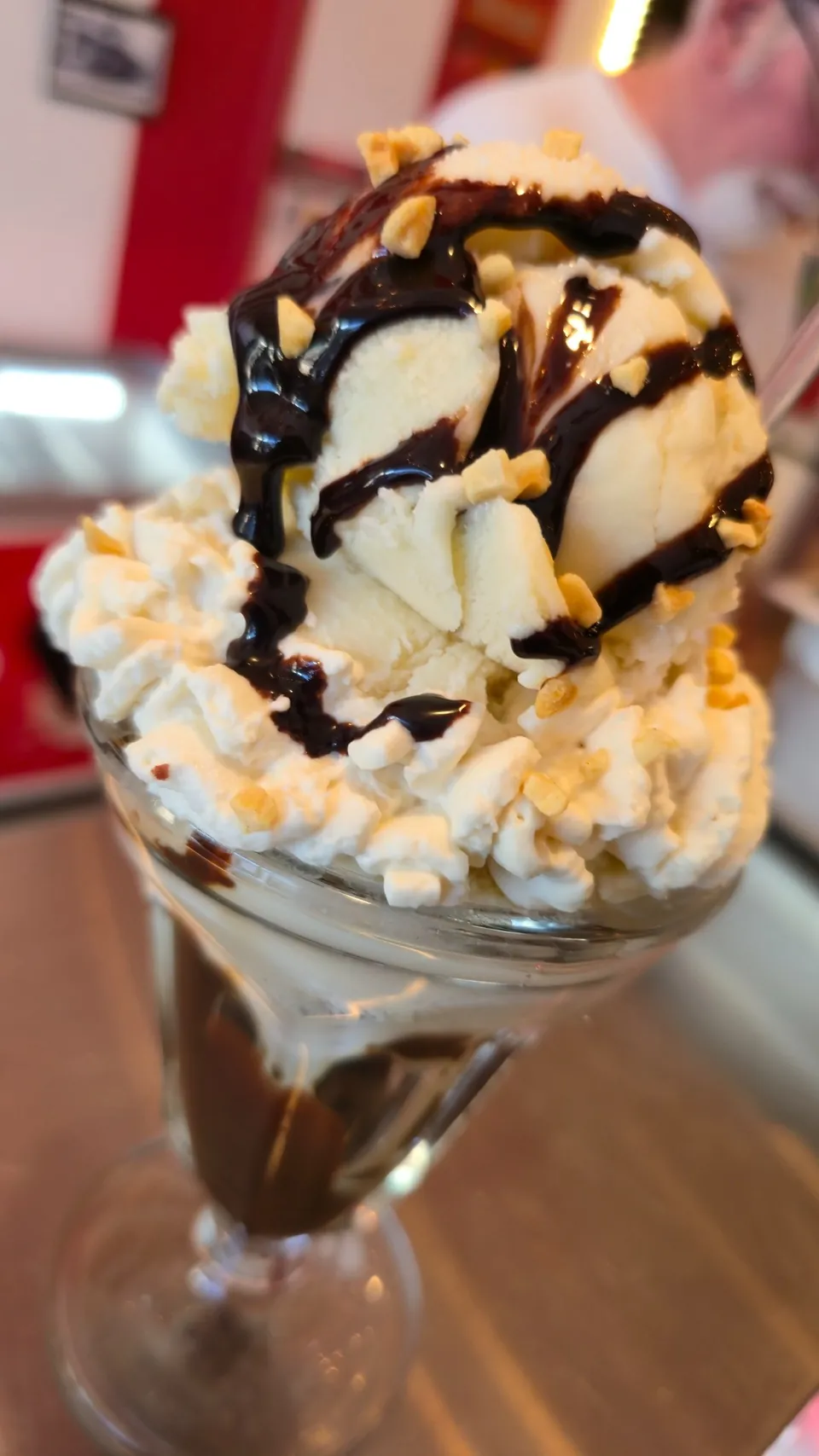 Hot fudge sundae with whipped cream and crushed nuts in a classic sundae glass