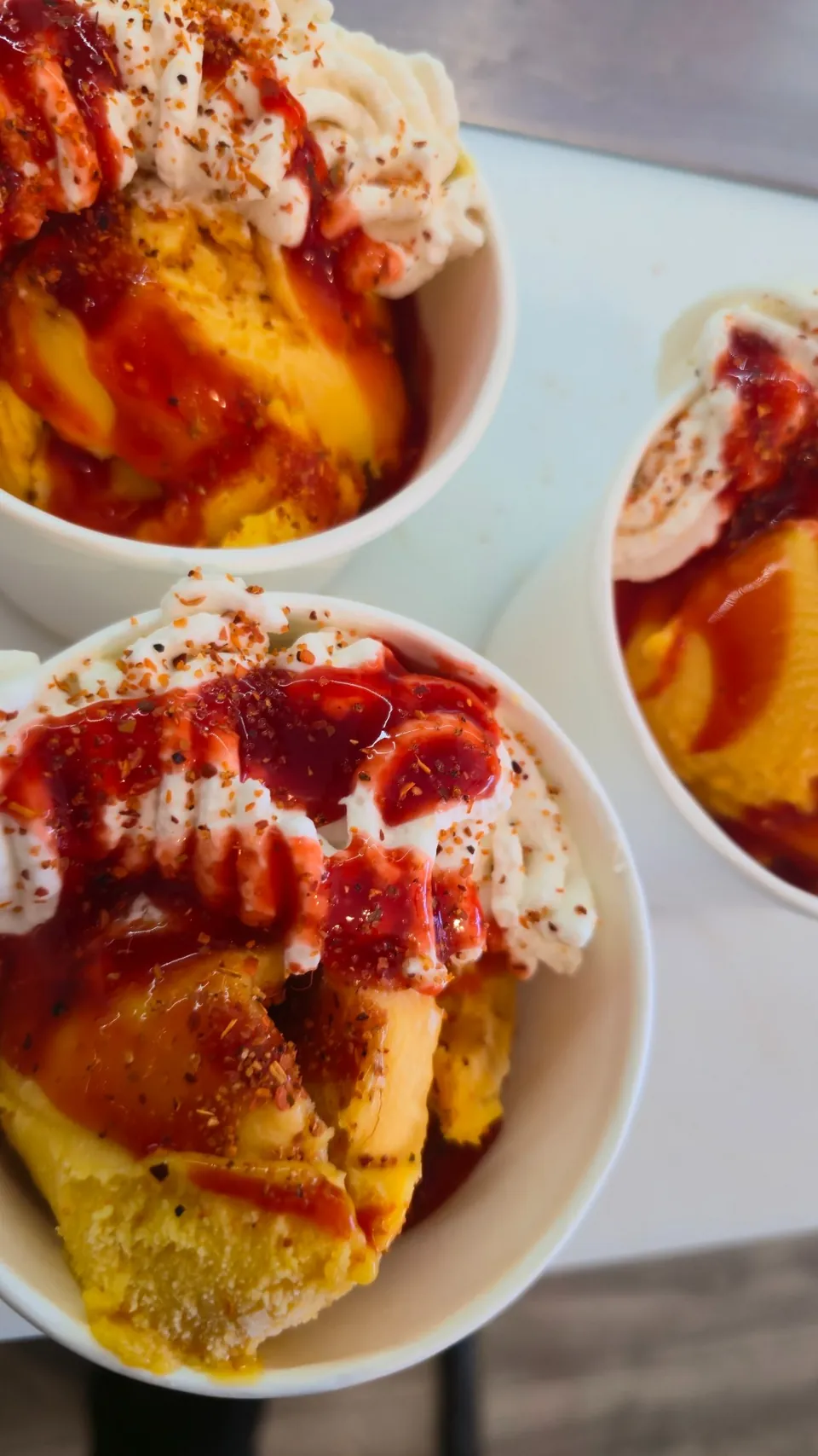 Three bowls of peach ice cream with strawberry drizzle and a dusting of cinnamon