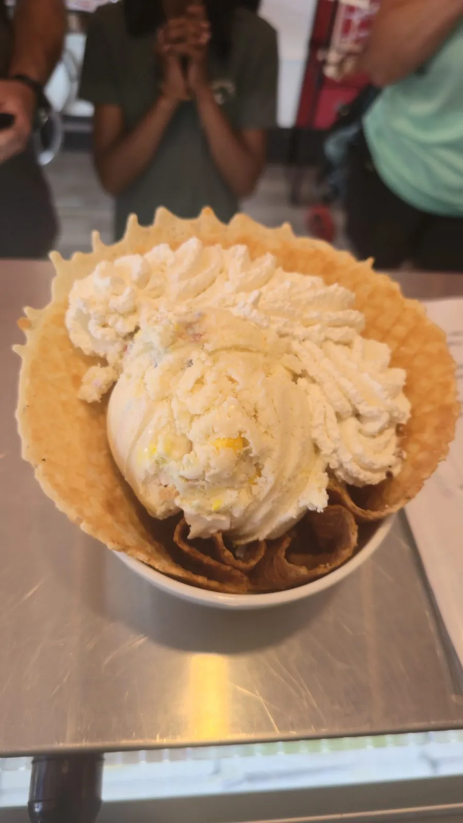 Vanilla ice cream scoop in a waffle bowl topped with whipped cream and sprinkles